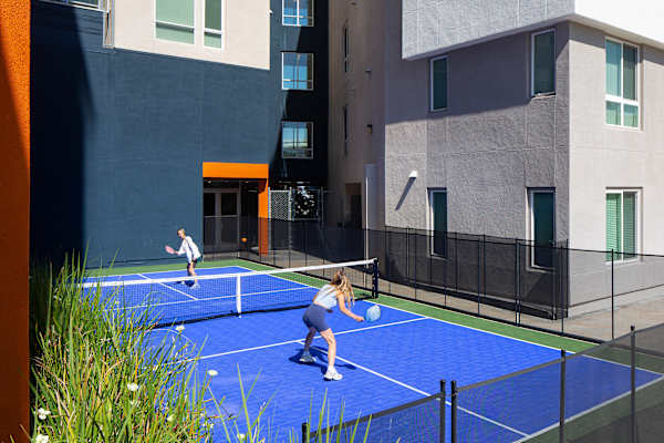 two women playing tennis on a blue court in front of a building